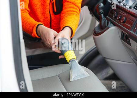 Sedile anteriore in tessuto per auto con aspirapolvere per uomo. uomo che pulisce la macchina da lavoro Foto Stock