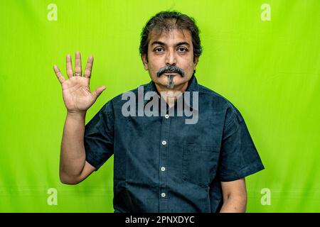 Un Signore ben vestito in camicia nera sta indicando 'cinque' con le dita della sua mano destra, in piedi contro uno sfondo verde schermo Foto Stock