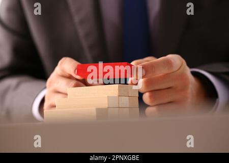 Mano d'uomo d'affari costruisce una scala da blocchi di legno in cima al colore rosso Foto Stock