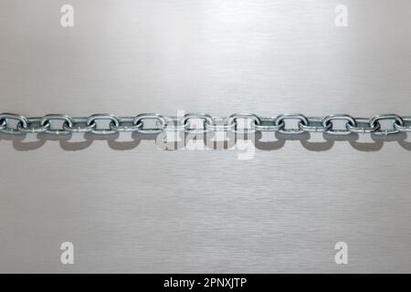 Vista dall'alto della catena metallica lucida con anelli d'argento di forma rotonda e ombra su sfondo grigio chiaro Foto Stock