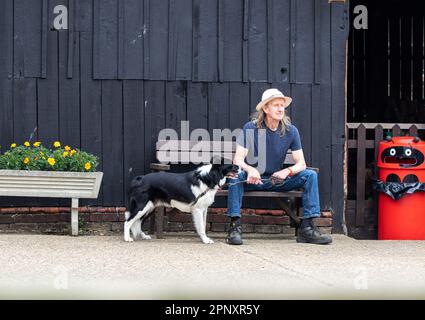 L'uomo ad un festival di musica in Suffolk rurale prende un momento tranquillo con il suo cane e seduto su una panchina per due. Foto Stock