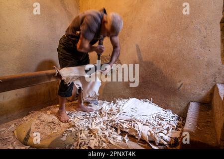 Un operaio nelle concerie di Fez ammorbidisce le pelli già conciate con un attrezzo speciale che viene spinto con il petto. Foto Stock