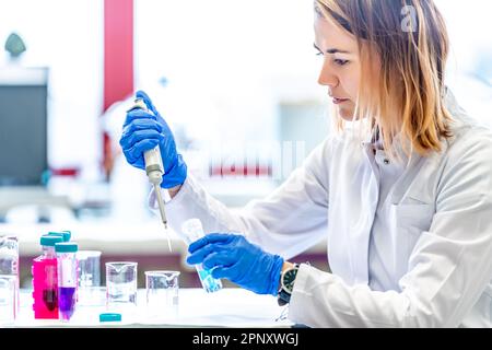 miscelazione di sostanze chimiche da parte di una giovane scienziata femminile in un laboratorio di ricerca universitario. sviluppo di nuovi farmaci e prodotti Foto Stock