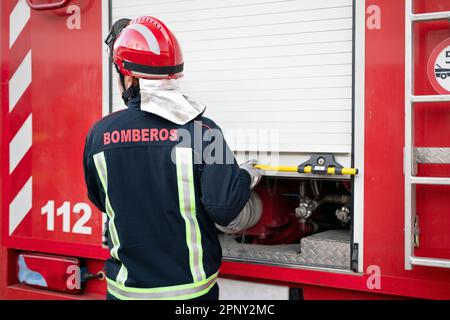 Pompiere in casco uniforme e protettivo, apertura armadio, preparazione per l'azione. Camion dei pompieri in background. Fotografia di alta qualità. Foto Stock