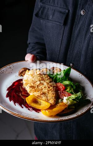 un uomo tiene un piatto in cui un pollo schnitzel. ristorante uomo Foto Stock