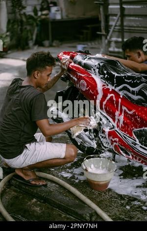 Uomo asiatico lavaggio moto con sapone alla stazione di servizio. Foto Stock