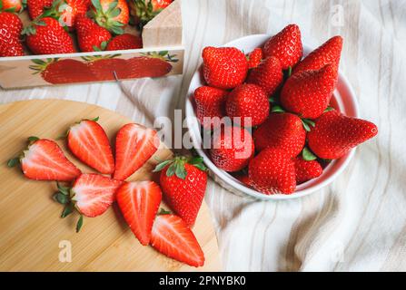 Fragole succose - intere in una ciotola e tagliate su una tavola Foto Stock