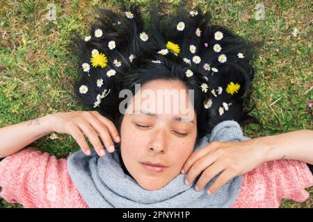 Una donna che giace sull'erba con i fiori nei suoi capelli, gli occhi chiusi e rilassato.concetto di primavera relax e connessione con la natura. Vista dall'alto. Foto Stock