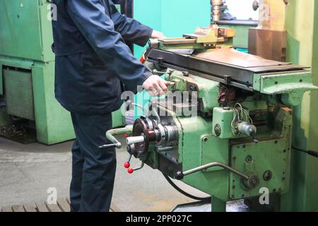 Un lavoratore maschio lavora su un più grande fabbro di ferro tornio, attrezzature per riparazioni, lavori di metallo in un'officina in un impianto metallurgico in un produ di riparazione Foto Stock