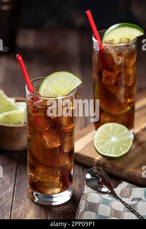 Cocktail al rum e alla cola in bicchieri alti con fettina di lime su un rustico tavolo di legno Foto Stock