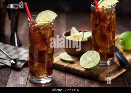 Cocktail al rum e alla cola in bicchieri alti con fettina di lime su un rustico tavolo di legno Foto Stock