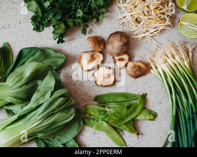 Ingredienti per la cucina asiatica: bok choy, funghi shiitake, germogli, lime, coriandolo, piselli verdi e cipolle verdi su un backgroun grigio di cemento Foto Stock