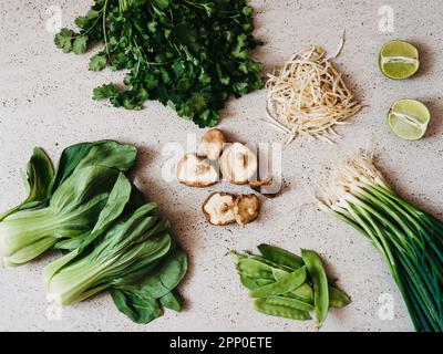 Ingredienti per la cucina asiatica: bok choy, funghi shiitake, germogli, lime, coriandolo, piselli verdi e cipolle verdi su un backgroun grigio di cemento Foto Stock