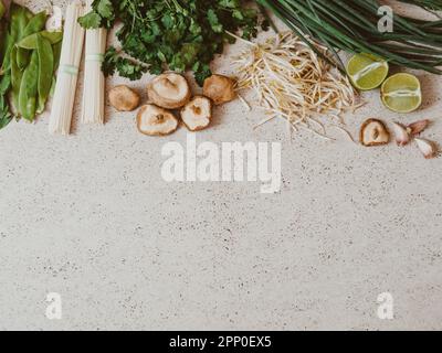 Ingredienti per la cucina asiatica: bok choy, funghi shiitake, germogli, lime, coriandolo, soba, piselli verdi e cipolle verdi su un cemento grigio bac Foto Stock