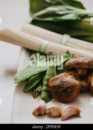 Ingredienti per la cucina asiatica: bok choy, funghi shiitake, soba, piselli verdi e aglio su piatto. Messa a fuoco selettiva. Vista frontale. Foto Stock