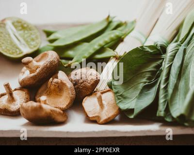 Ingredienti per la cucina asiatica: bok choy, funghi shiitake, soba, piselli verdi e aglio su piatto. Messa a fuoco selettiva. Vista frontale. Foto Stock