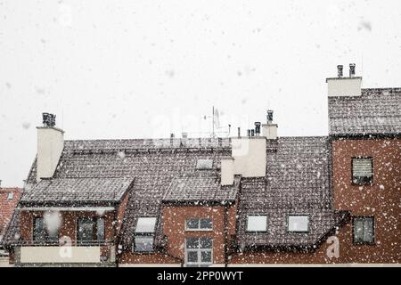 Neve bianca, grandi fiocchi di neve in caduta, vista del tetto dell'edificio con antenne montate e tubi di ventilazione contro il cielo grigio Foto Stock