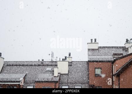 Neve bianca, grandi fiocchi di neve in caduta, vista del tetto dell'edificio con antenne montate e tubi di ventilazione contro il cielo grigio Foto Stock