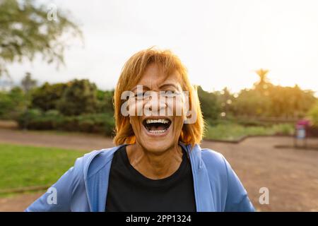 Felice donna latina anziana che si diverte sorridendo sulla macchina fotografica dopo l'attività di allenamento in un parco pubblico Foto Stock