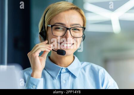 Ritratto di una donna di successo che si è occupata dell'assistenza clienti online, di una donna d'affari che sorride e guarda la fotocamera, di uno specialista dell'assistenza telefonica che utilizza le cuffie per videochiamare e consultare i clienti. Foto Stock