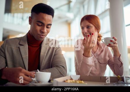 Un giovane uomo d'affari sta avendo un colloquio amichevole con la collega mentre si gustano il caffè dopo un pranzo in un'atmosfera piacevole in azienda b Foto Stock