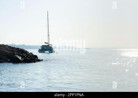 Catamarano ancorato al largo della costa rocciosa di Ses Illetes, con la città di Palma sullo sfondo, all'alba Foto Stock