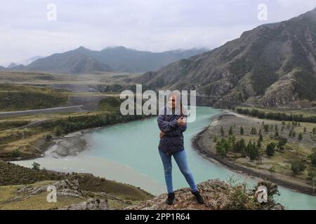 Giovane donna in piedi vicino alla confluenza di due fiumi di diversi colori Chuya e Katun in uno. Paesaggio montano, Repubblica Altai, Russia. Alto qual Foto Stock