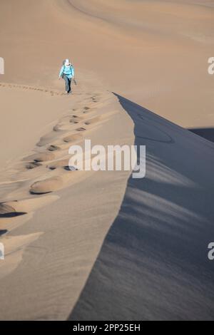 Donna che si arrampica sulla cresta di una duna nella zona di Erg Chegaga. Foto Stock