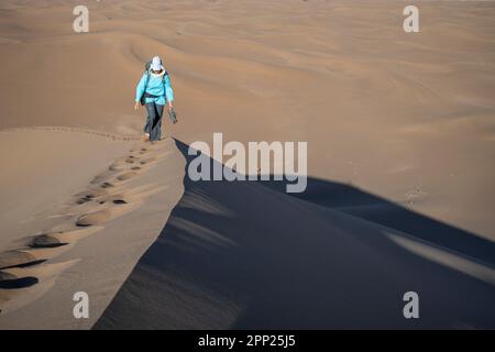 Donna che si arrampica sulla cresta di una duna nella zona di Erg Chegaga. Foto Stock