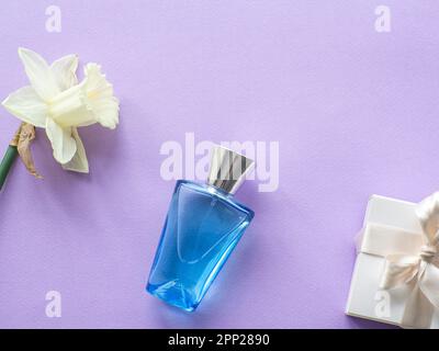 Confezione regalo bianca e bottiglia di profumo con narcoschi su fondo lilla con spazio copia. Concetto di dare un regalo alle donne, madri giorno holid Foto Stock