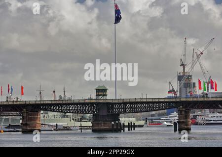 602 il ciclista e il ponte pedonale Pyrmont Bridge attraverso Cockle Bay a Darling Harbour-enorme bandiera nazionale. Sydney-Australia. Foto Stock