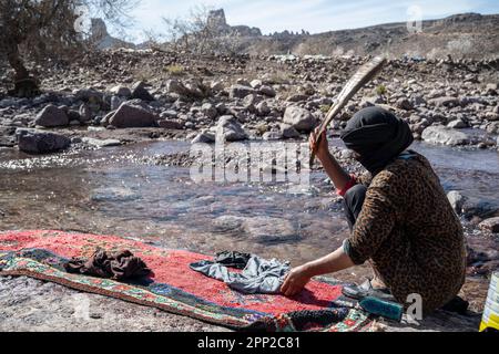 Donna berbera che lava i vestiti a mano nel fiume con i pinnacoli di Babn Ali sullo sfondo. Foto Stock