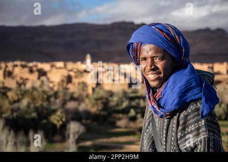 Ritratto di un giovane vestito con gli abiti tipici dei nomadi berberi accanto ad un punto di vista sull'oasi di Tinghir. Foto Stock