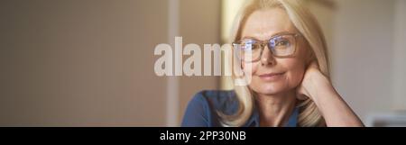 Ritratto interno di attraente donna matura con piacevole sorriso rilassante sul divano nel suo appartamento moderno Foto Stock