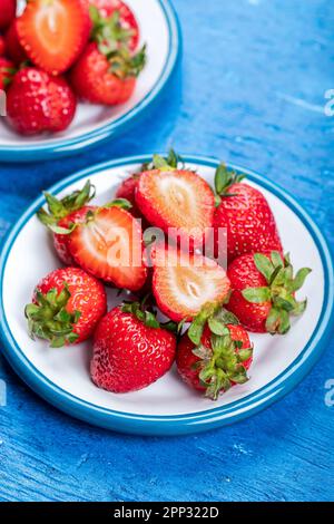 Fragole fresche su piatti bianchi, su fondo di legno blu. Foto Stock