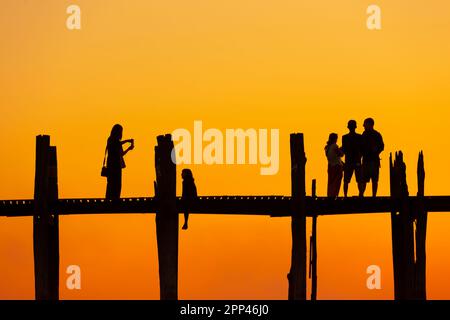 Amarapura, Myanmar - 22 novembre 2016: Persone non identificate camminano sul ponte U Bein al tramonto in Myanmar. Il ponte U Bein è il ponte in teak più lungo del Th Foto Stock