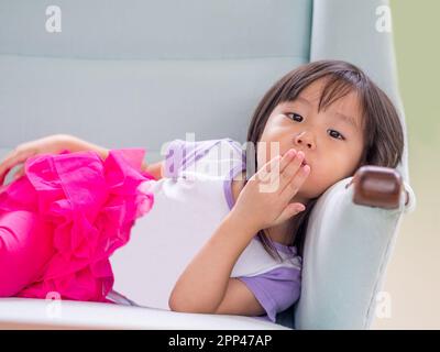 Bella bambina che si posa su un divano bianco a casa, ragazza asiatica Foto Stock