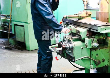 Un lavoratore maschio lavora su un più grande fabbro di ferro tornio, attrezzature per riparazioni, lavori di metallo in un'officina in un impianto metallurgico in un produ di riparazione Foto Stock