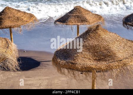 Ombrelloni da spiaggia di paglia lungo una splendida costa al crepuscolo. Foto Stock