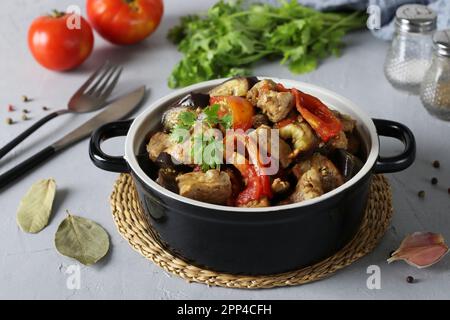 Maiale brasato con melanzane e pomodori in piatto di ceramica su fondo grigio chiaro Foto Stock
