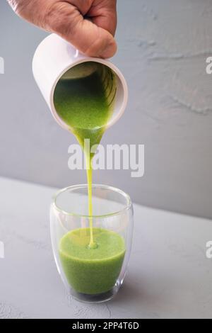 Frullato verde o zuppa fatta di erbe e verdure selvatiche è versato in un bicchiere da bere a doppia parete su uno sfondo grigio, conce cibo sano Foto Stock