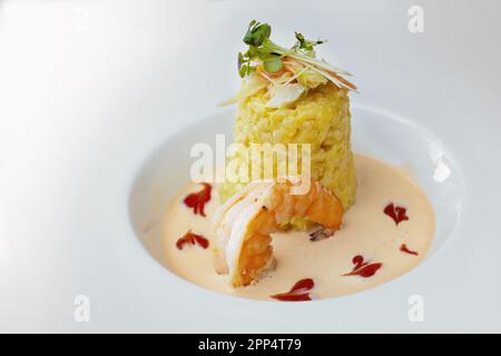 Piatto gourmet di risotto allo zafferano con farcitura di verdure e erbe, un grande sugo di gamberi e crostacei in un moderno piatto bianco, spazio copia, selezionato fo Foto Stock