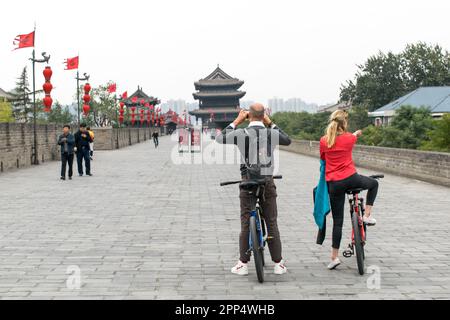 Il retro di una coppia di turisti, un uomo e una donna, si fermano sulle mura della città di Xi'an mentre si pedala per scattare una foto. Foto Stock
