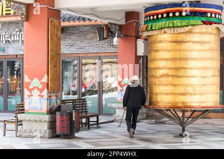 Un anziano tibetano gira una ruota di preghiera tibetana di dimensioni umane - Kanding, Cina. Foto Stock