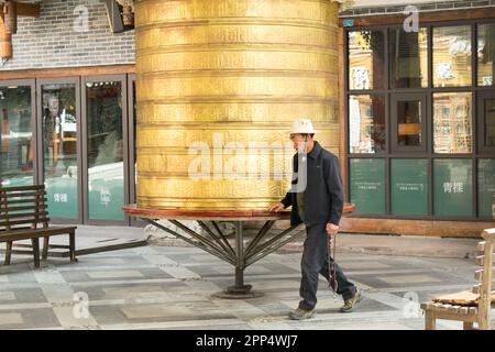 Un anziano tibetano gira una ruota di preghiera tibetana di dimensioni umane - Kanding, Cina. Foto Stock