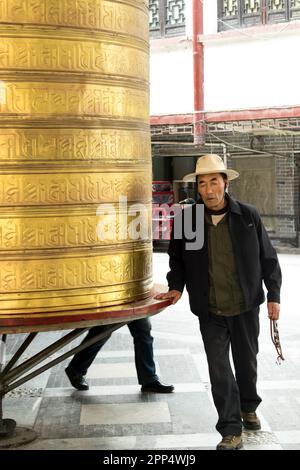 Un anziano tibetano gira una ruota di preghiera tibetana di dimensioni umane - Kanding, Cina. Foto Stock