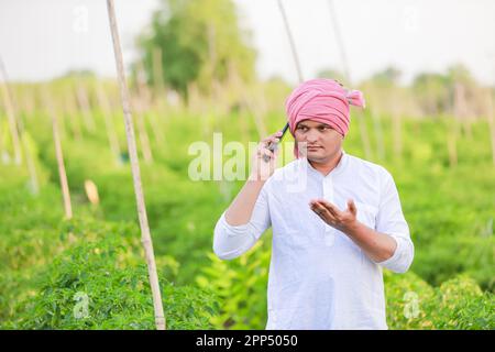 Giovane agricoltore indiano che mostra smartphone, agricoltore che parla al telefono in fattoria, agricoltore indiano felice Foto Stock