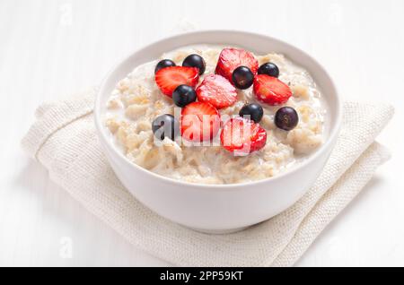 Gustoso porridge con fettine di fragole e ribes nero in ciotola Foto Stock