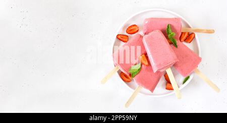 Il gelato alla fragola si apre su un piatto bianco su sfondo di pietra bianca con spazio libero per il testo. Vista dall'alto, disposizione piatta Foto Stock