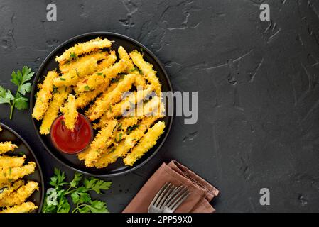 Le zucchine fritte si attaccano al piatto su sfondo nero con spazio libero per il testo. Vista dall'alto, disposizione piatta Foto Stock